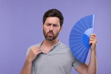 Photo of Unhappy man with hand fan suffering from heat on purple background