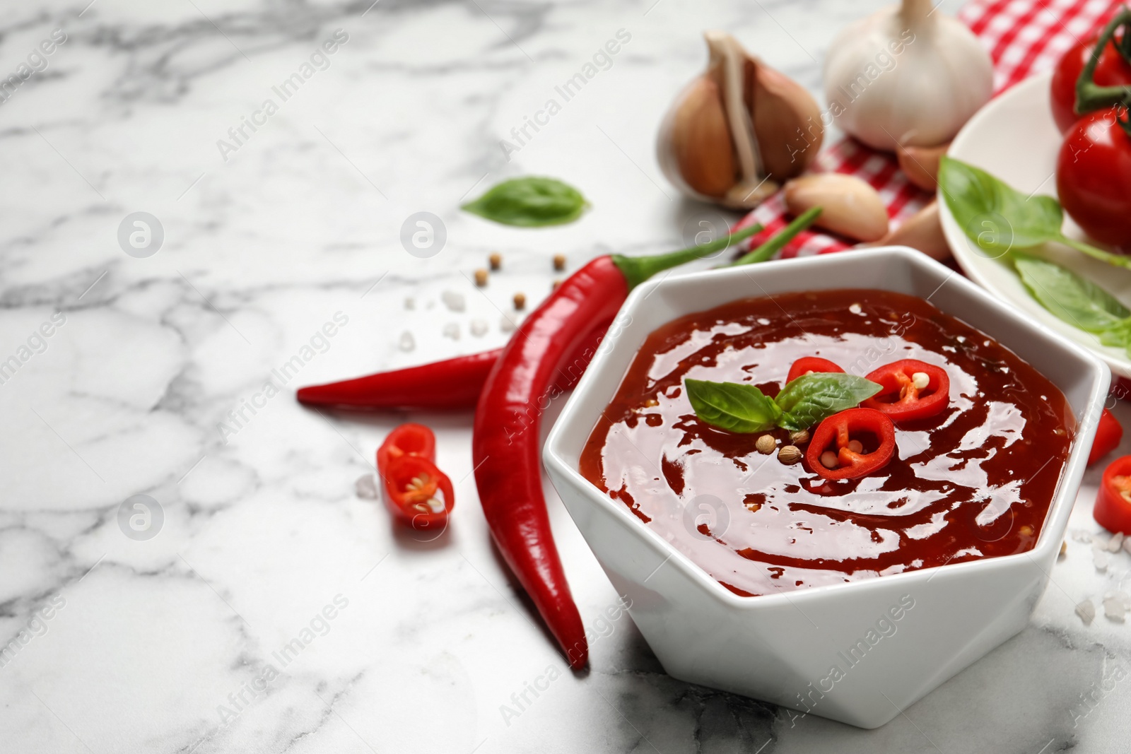 Photo of Spicy chili sauce with basil in bowl on white marble table, space for text