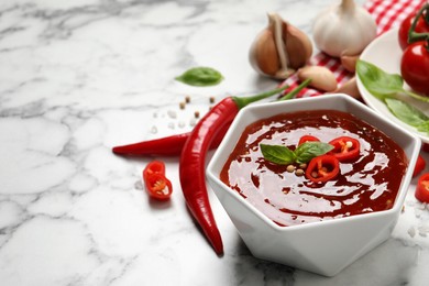 Spicy chili sauce with basil in bowl on white marble table, space for text