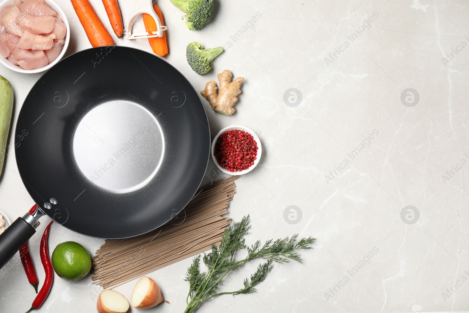 Photo of Empty iron wok surrounded by raw ingredients on light table, flat lay. Space for text