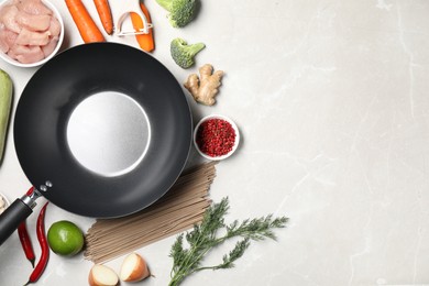 Photo of Empty iron wok surrounded by raw ingredients on light table, flat lay. Space for text