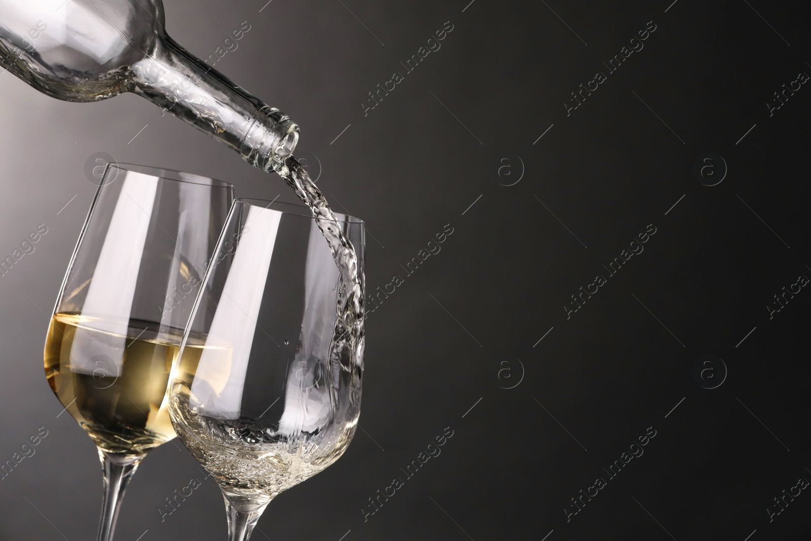 Photo of Pouring white wine into glass against grey background, closeup. Space for text