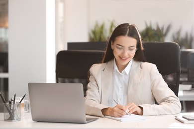 Photo of Happy woman using modern laptop at white desk in office