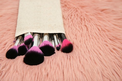 Photo of Bag with set of professional makeup brushes on furry fabric. Space for text