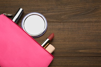 Stylish pocket mirror and cosmetic bag with makeup products on wooden table, flat lay. Space for text