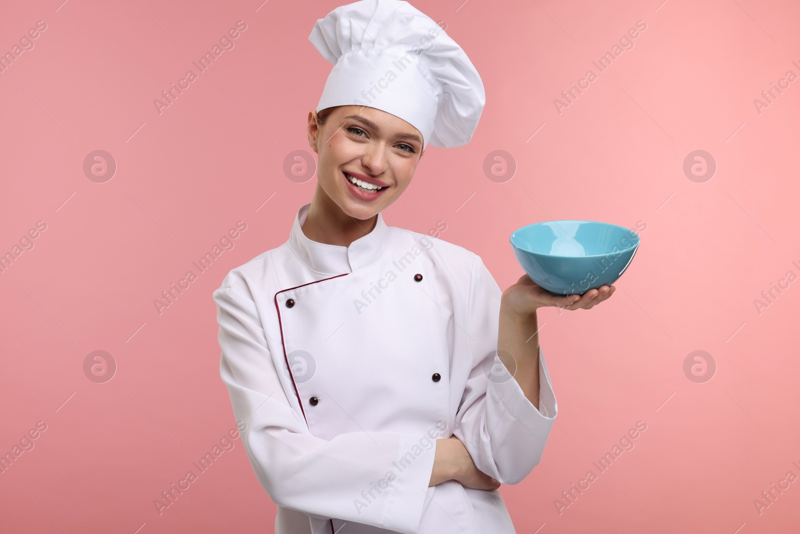 Photo of Happy chef in uniform holding bowl on pink background