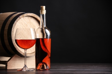 Photo of Wooden cask, bottle and glass of wine on table against dark background, space for text