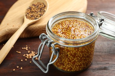 Whole grain mustard in jar on wooden table, closeup