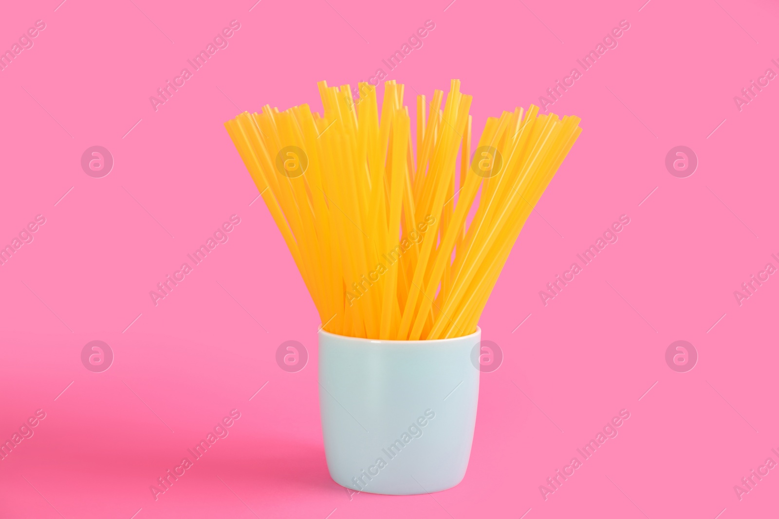Photo of Yellow plastic drinking straws in holder on pink background