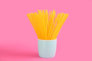 Photo of Yellow plastic drinking straws in holder on pink background