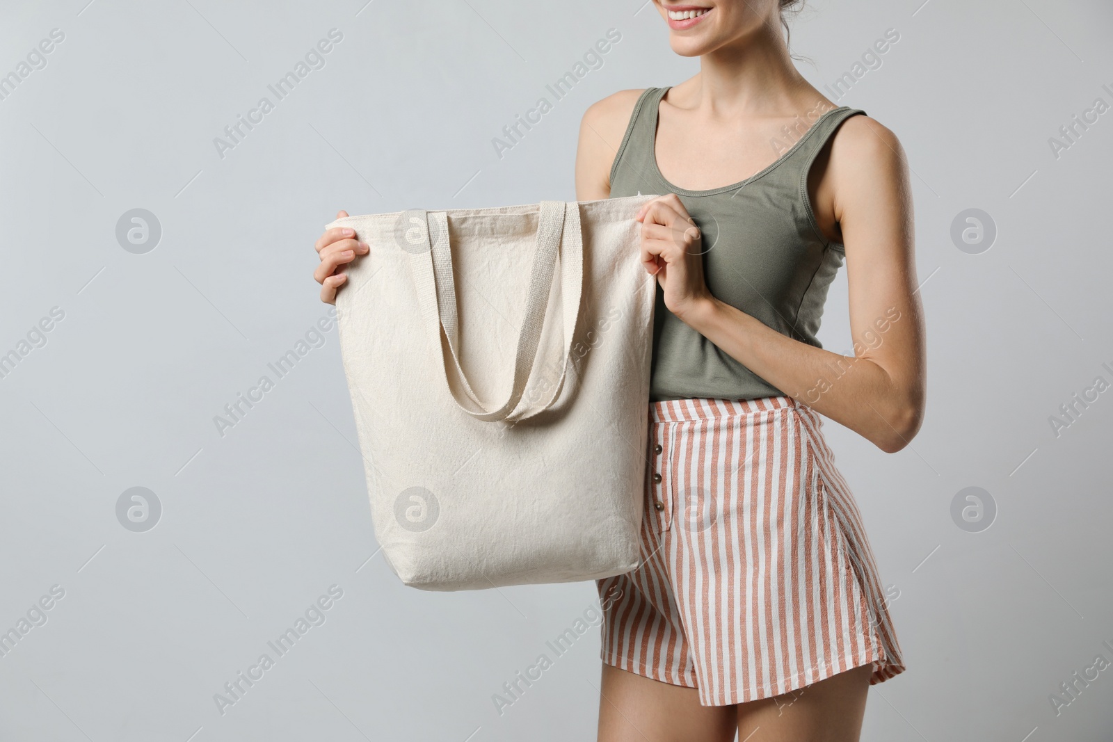 Photo of Happy young woman with blank eco friendly bag on light background, closeup