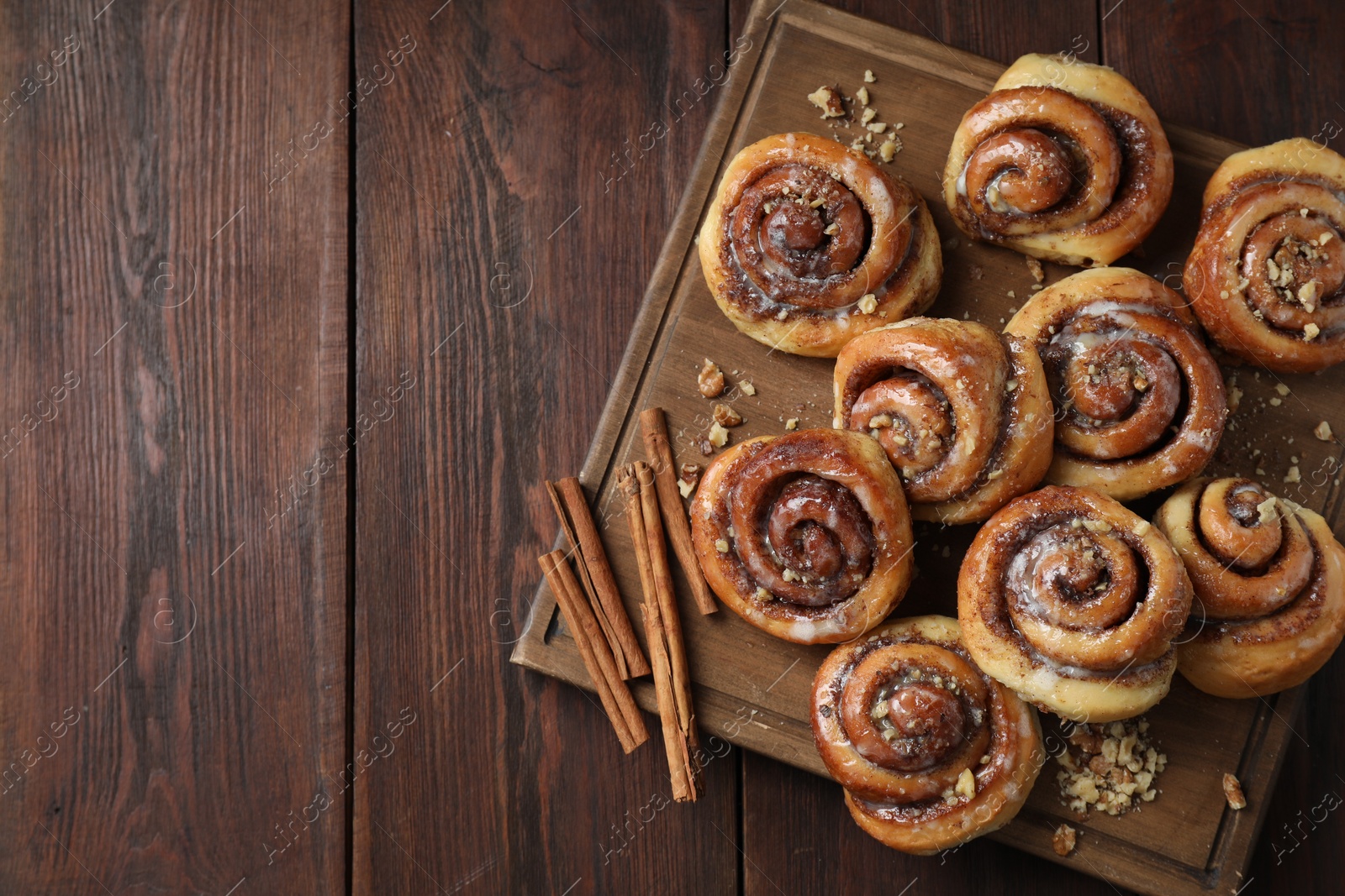 Photo of Tasty cinnamon rolls, sticks and nuts on wooden table, top view. Space for text