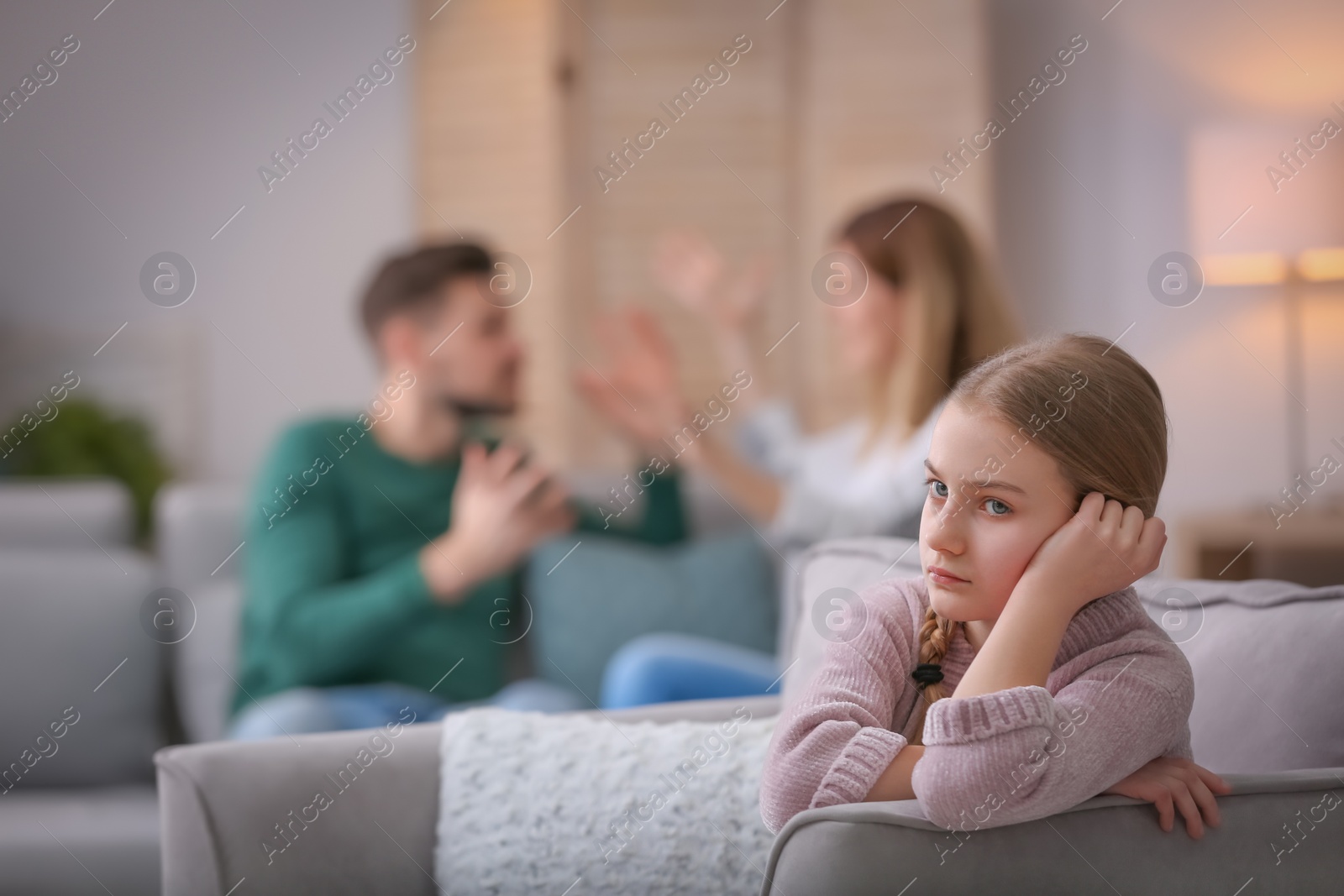 Photo of Little unhappy girl sitting in armchair while parents arguing at home