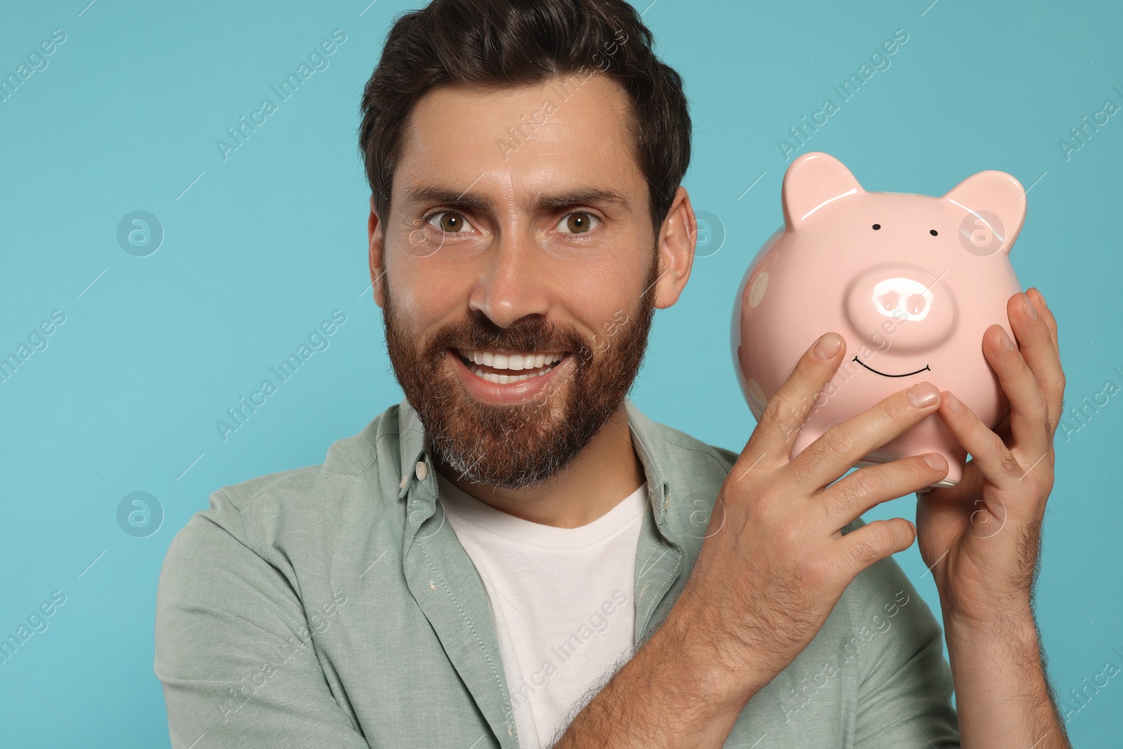 Photo of Happy man with ceramic piggy bank on light blue background