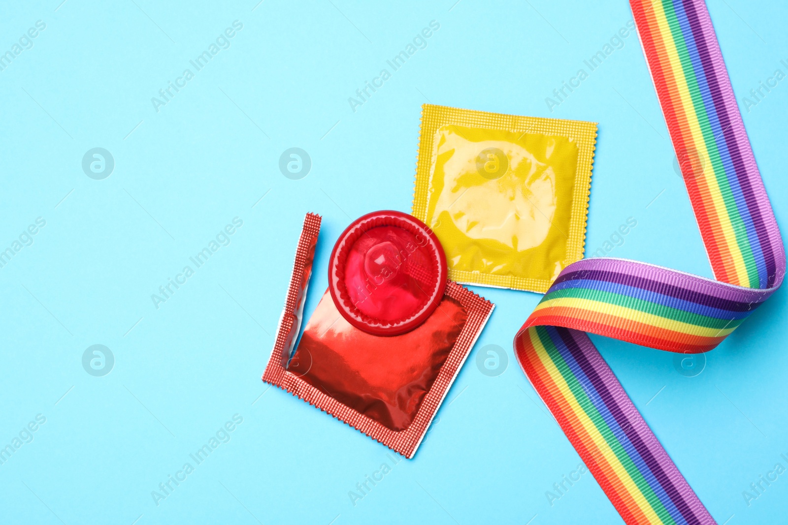 Photo of Colorful condoms and rainbow ribbon on light blue background, flat lay. LGBT concept