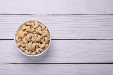 Tasty cashew nuts in bowl on white wooden table, top view. Space for text