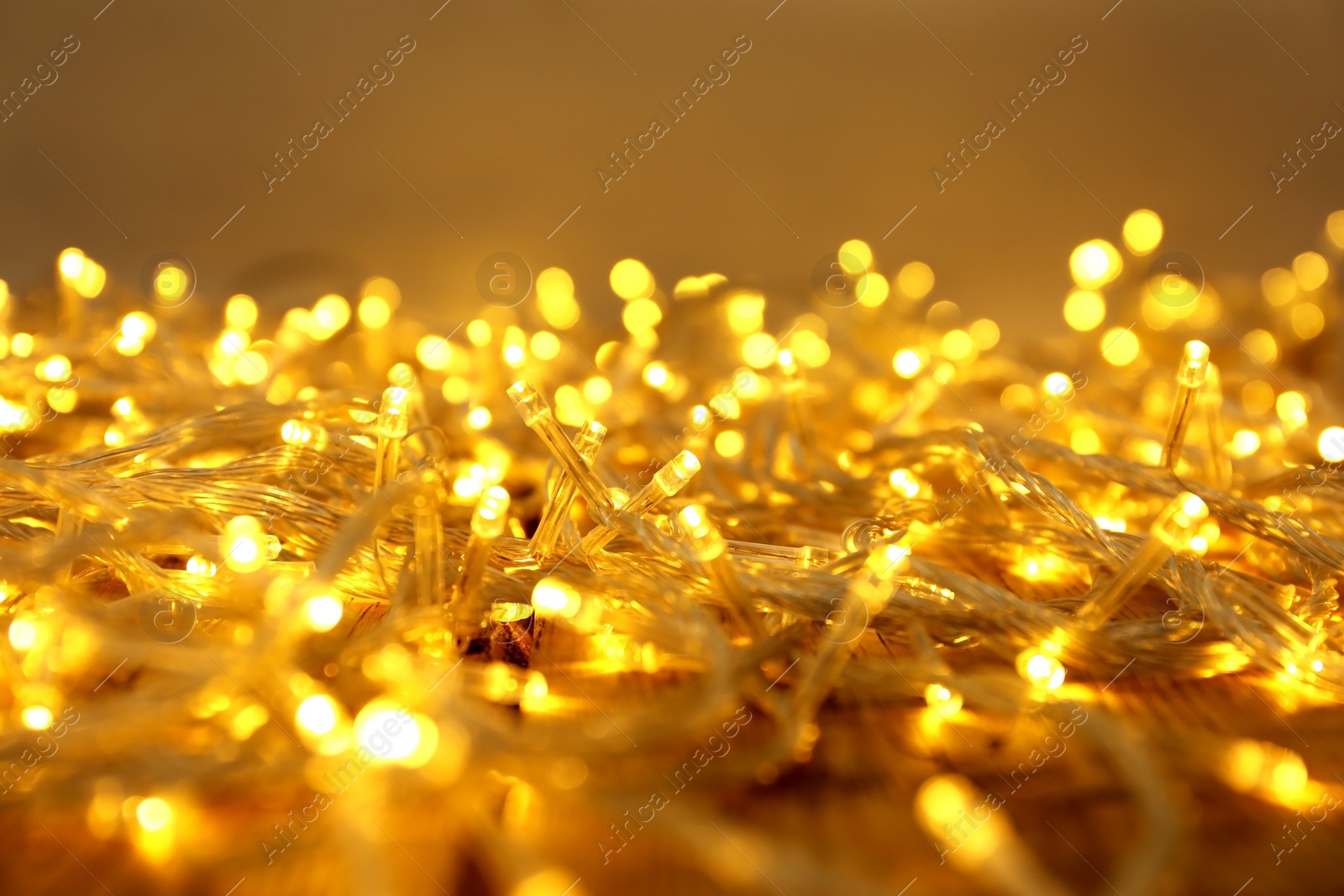 Photo of Glowing Christmas lights on wooden table, closeup