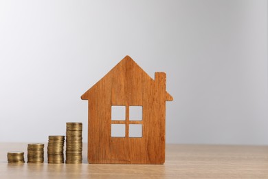 Photo of Mortgage concept. Model house and stacks of coins on wooden table against light grey background, space for text