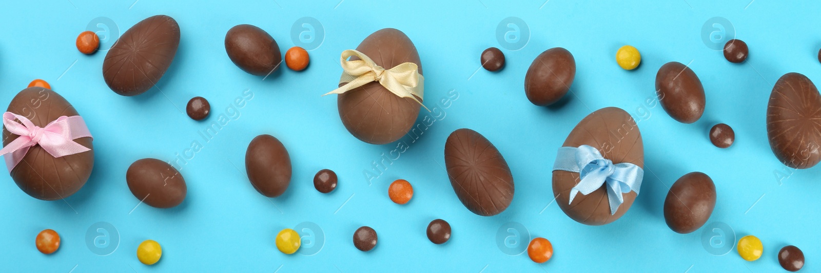 Image of Sweet chocolate eggs and bright candies on light blue background, flat lay. Banner design