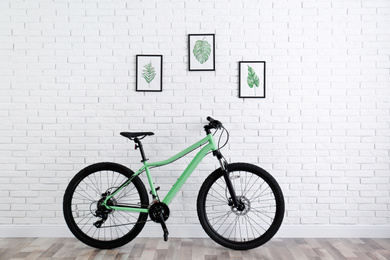 Photo of Modern green bicycle near white brick wall indoors