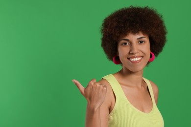 Photo of Happy young woman pointing at something on green background. Space for text