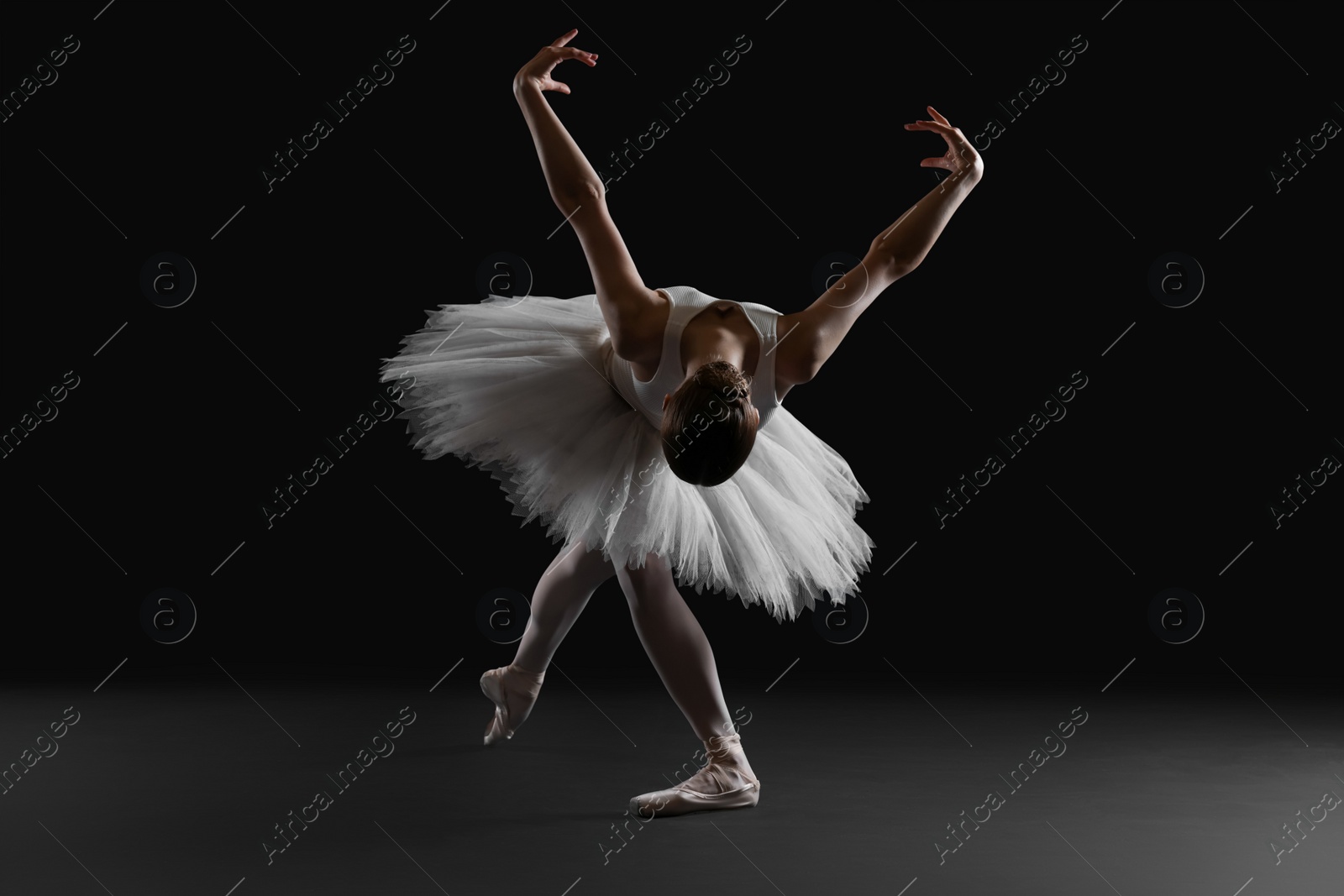 Photo of Young ballerina practicing dance moves on black background