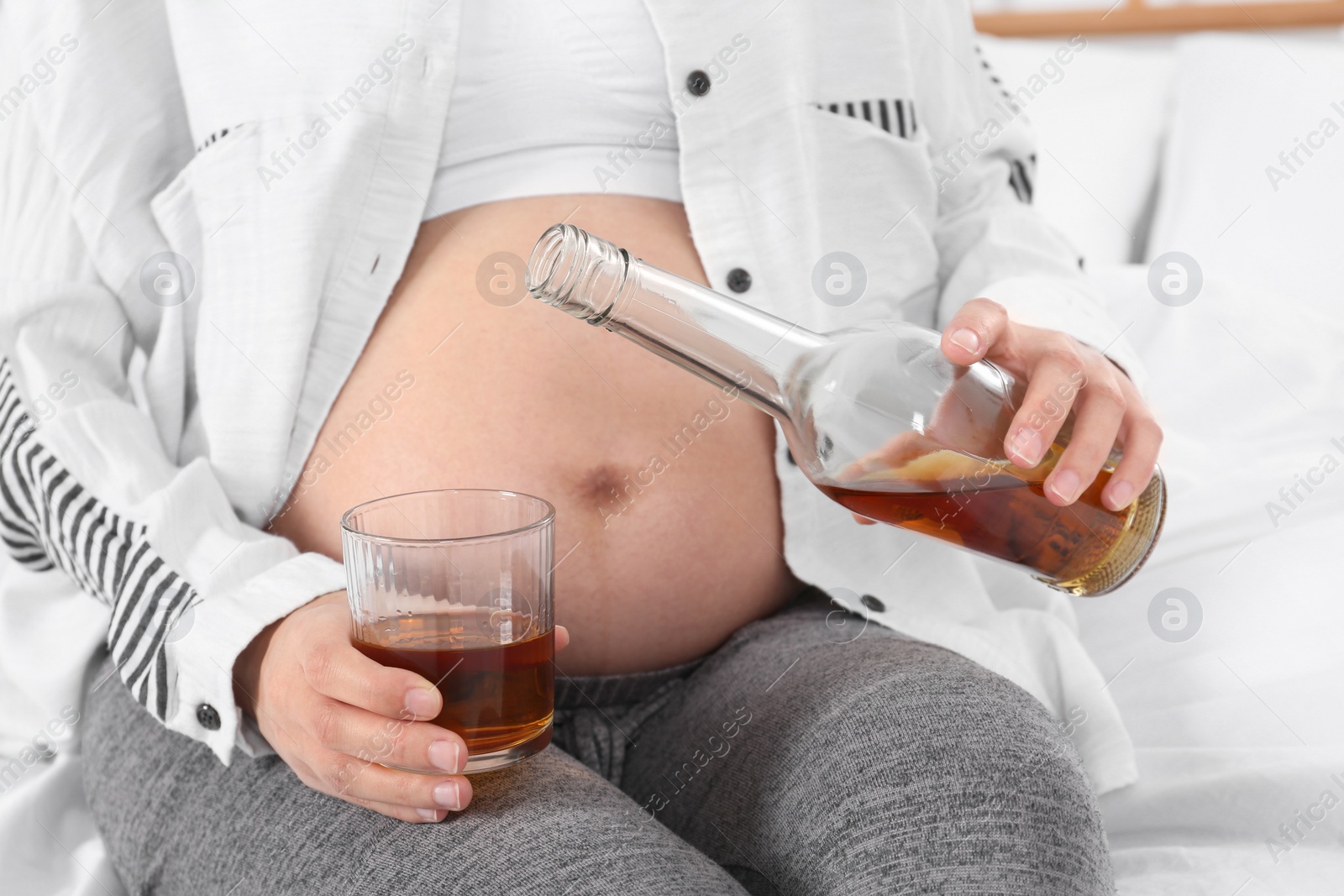 Photo of Pregnant woman pouring whiskey into glass at home. Alcohol addiction