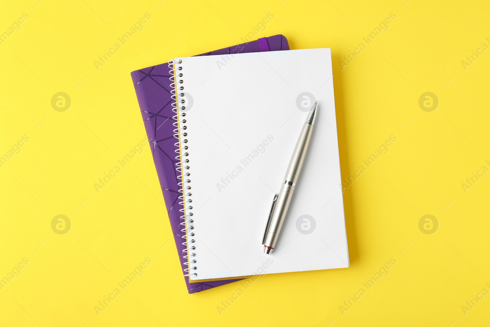 Photo of Notebooks and pen on yellow background, top view