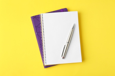 Photo of Notebooks and pen on yellow background, top view