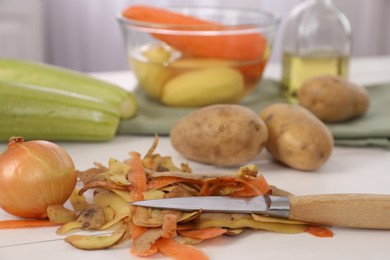 Peels of fresh vegetables and knife on white table, closeup