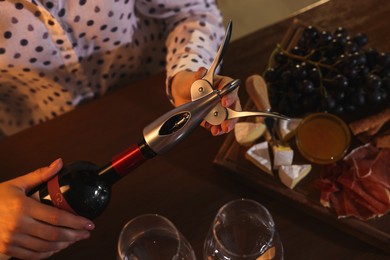 Romantic dinner. Woman opening wine bottle with corkscrew at table indoors, above view