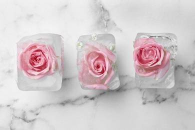 Photo of Ice cubes with roses on marble background, flat lay