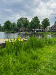 Photo of Beautiful view of city canal with pier and moored boat surrounded by greenery