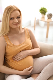 Beautiful pregnant woman sitting on sofa at home