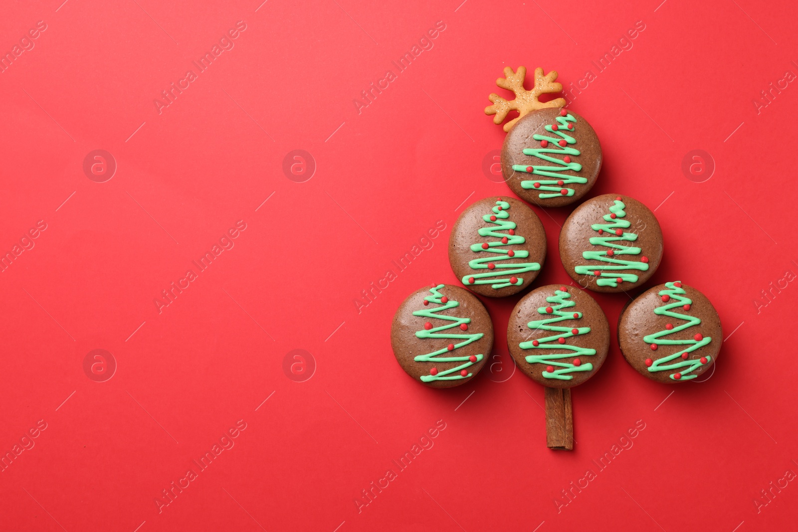 Photo of Beautifully decorated Christmas macarons on red background, flat lay. Space for text