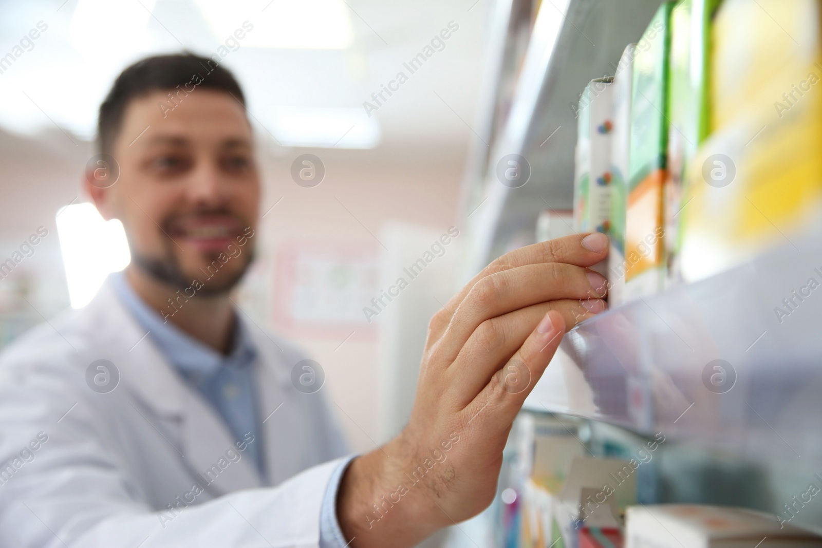 Photo of Professional pharmacist near shelves with merchandise in drugstore, focus on hand