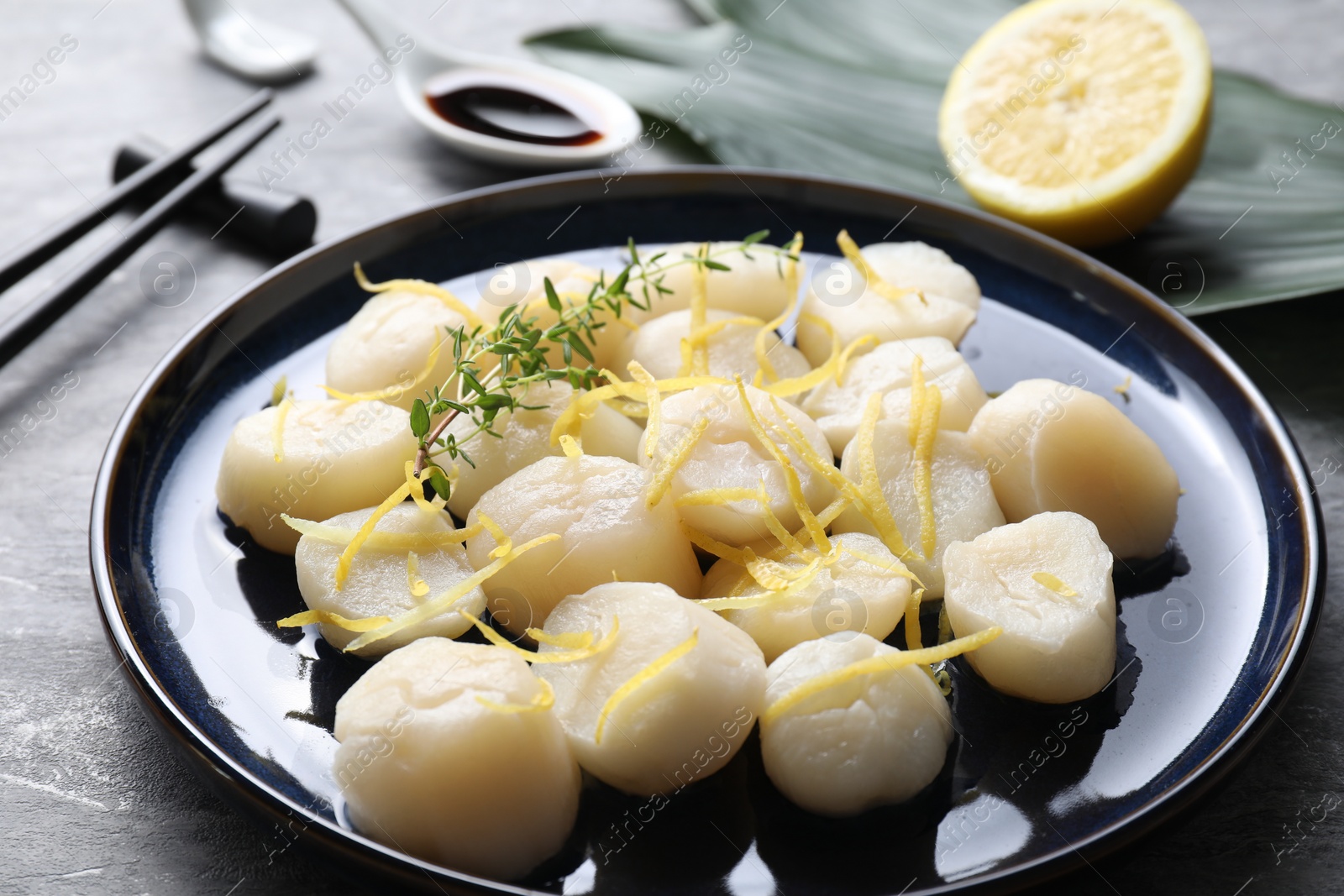 Photo of Raw scallops with thyme and lemon zest on grey table, closeup