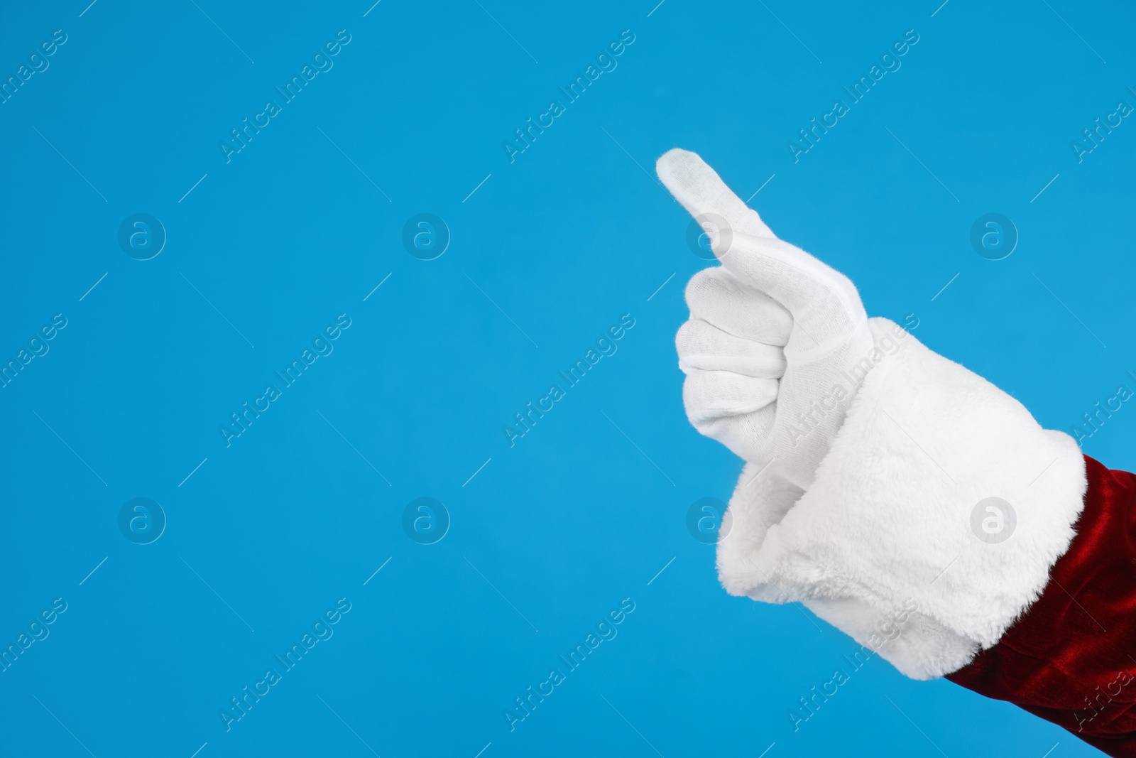 Photo of Santa Claus pointing at something on blue background, closeup of hand. Space for text