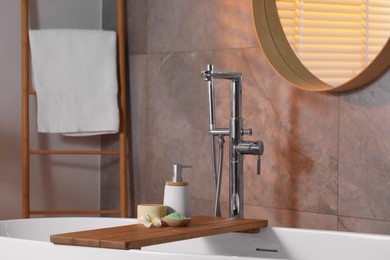 Photo of Spa products and beautiful flower on wooden tub tray in bathroom