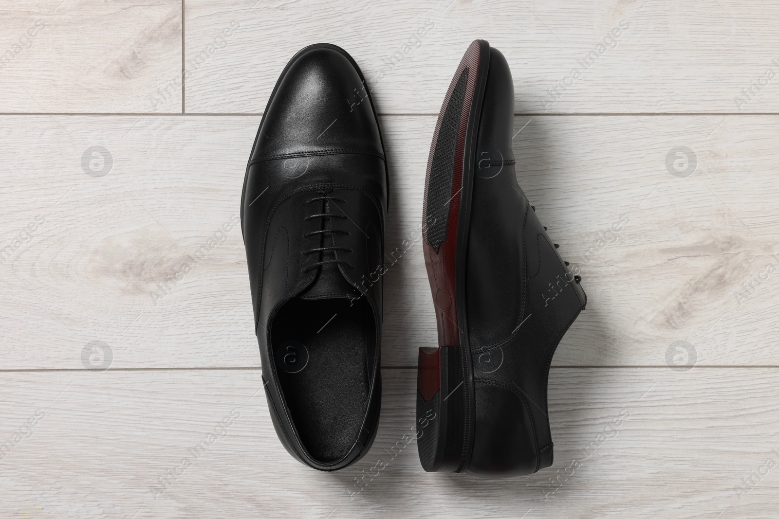 Photo of Pair of black leather men shoes on light wooden floor, top view