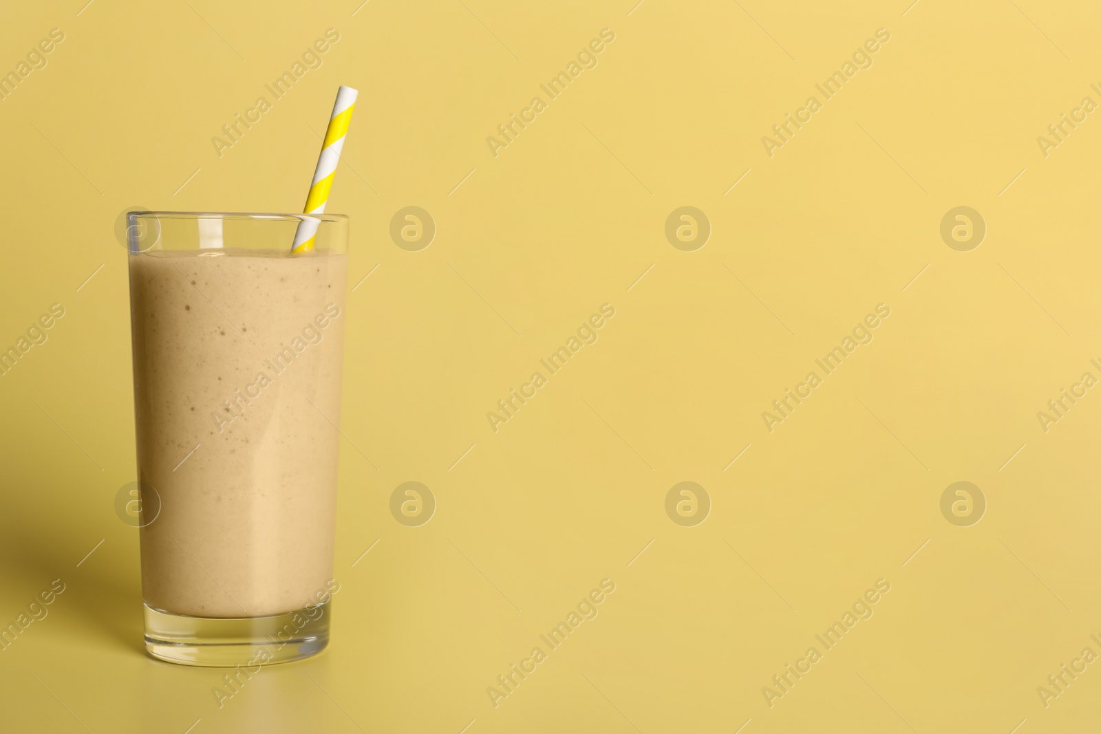 Photo of Glass of tasty smoothie with straw on pale yellow background. Space for text