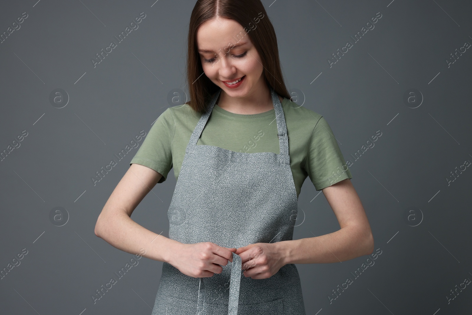 Photo of Beautiful young woman wearing kitchen apron on grey background. Mockup for design