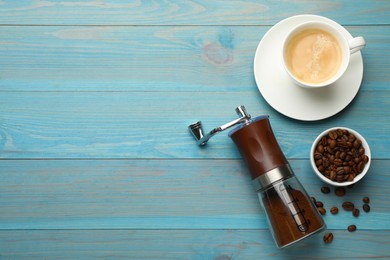 Manual coffee grinder with powder, beans and cup of drink on light blue wooden table, flat lay. Space for text