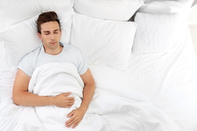 Photo of Young man sleeping on soft pillows in bed at home