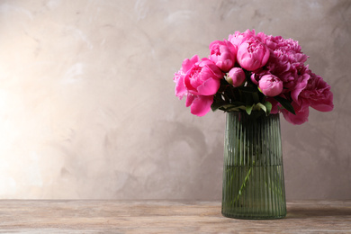 Photo of Beautiful peony bouquet in vase on wooden table against grey background. Space for text
