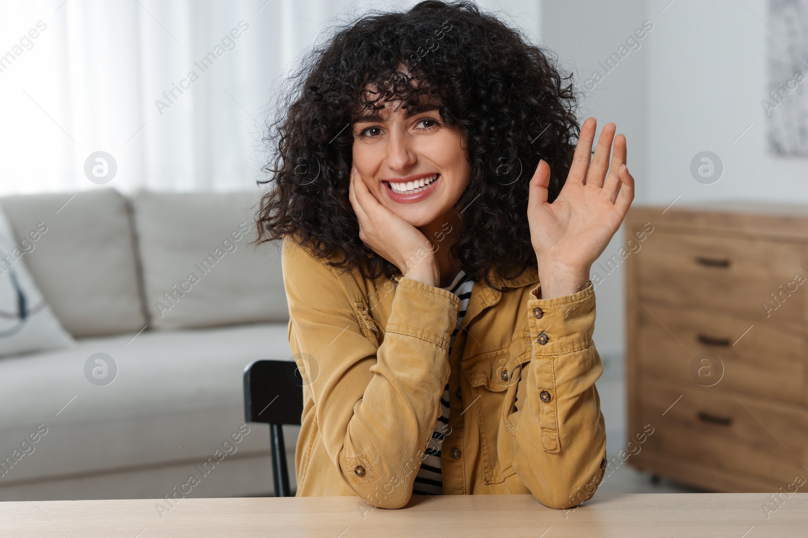 Photo of Happy woman waving hello at wooden table in room