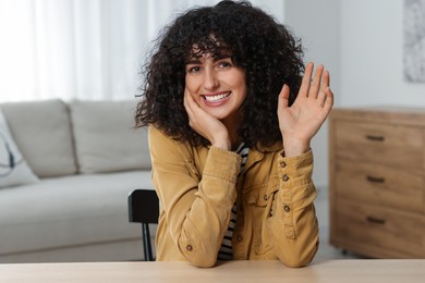 Happy woman waving hello at wooden table in room