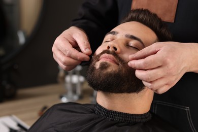Photo of Professional barber working with client's mustache in barbershop, closeup