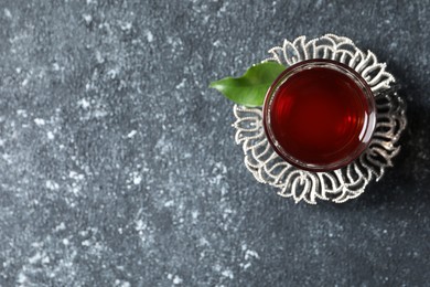 Photo of Glass of traditional Turkish tea in vintage holder on grey textured table, top view. Space for text
