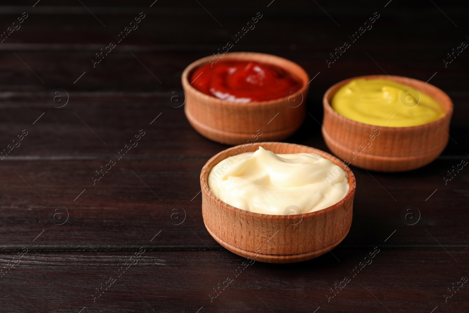 Photo of Ketchup, mustard and mayonnaise in bowls on wooden table, space for text